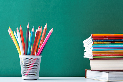 Image of crayons and exercise books against blackboard